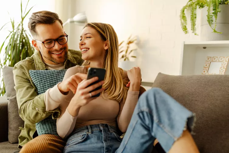 Happy couple sitting on a sofa, looking at a smartphone.