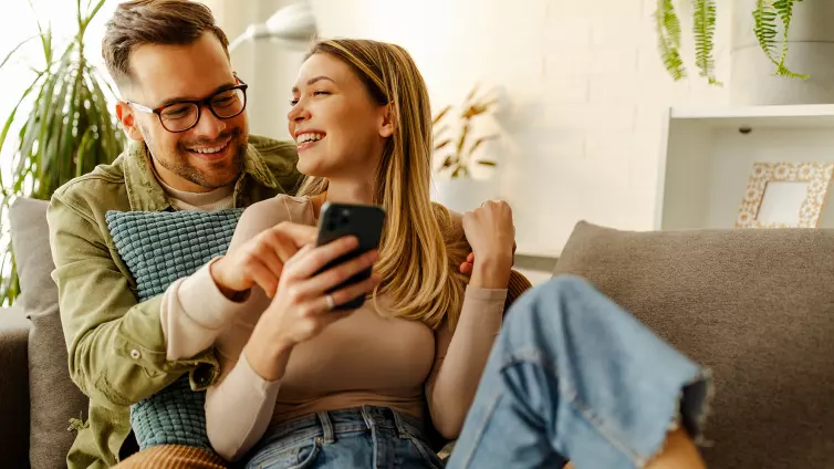 Happy couple sitting on a sofa, looking at a smartphone.