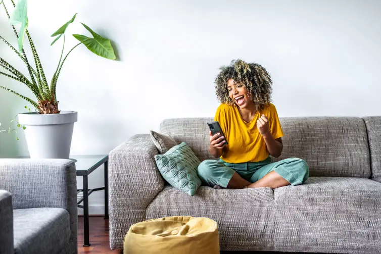 Woman sat on a sofa, looking at a phone, appears happy.