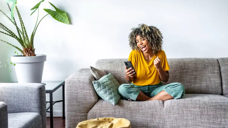 Woman sat on a sofa, looking at a phone, appears happy.