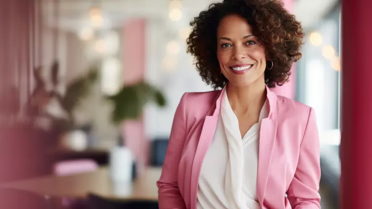 Business woman wearing pink blazer with office background.
