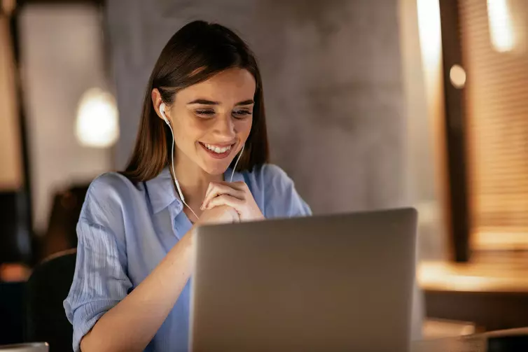 Woman wearing headphones looking at laptop smiling.