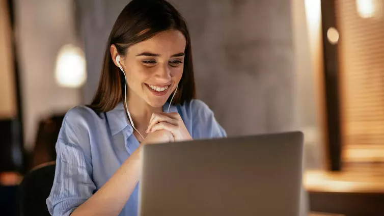 Woman wearing headphones looking at laptop smiling.