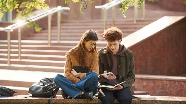 Sitting together. Man and woman students are outdoors near university.